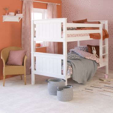White classic bunk bed in pink and orange themed bohemian girls room, with spotty wallpaper and bedding, wicker chair 