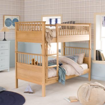Oak bunk bed with spindles and fitted ladder, in bedroom with check wallpaper and blue panelled wall underneath