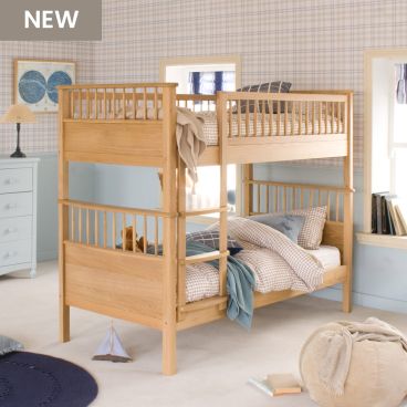 Oak bunk bed with spindles and fitted ladder, in bedroom with check wallpaper and blue panelled wall underneath