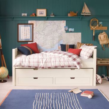 Space saving low sleeper child's bed with sleepover trundle and storage drawers underneath, in front of teal panelled wall and traditional child's bedroom with vintage accessories.