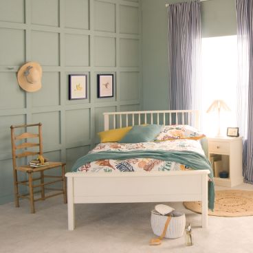 small double bed in white with spindles, with vintage wooden chair and bedside table next to it.
