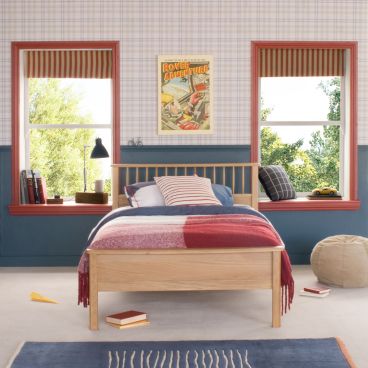 Oak small double bed with spindles, in traditional bedroom with blue panelled wall and wallpapered wall. Red architrave around windows and blue and red bedding on bed