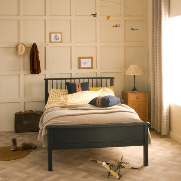 navy blue kids spindle bed with ochre gingham bedding, neutral panelled walls and aeroplane mobile 
