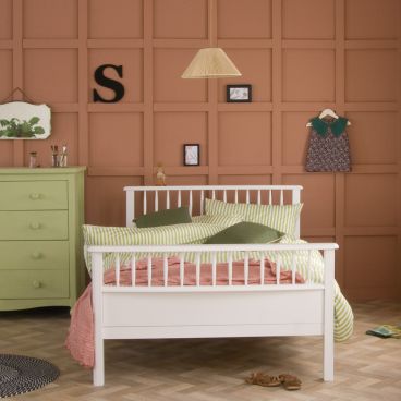 small double bed with terracotta panelling behind and green chest next to it 