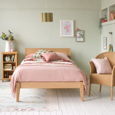 Sleek oak small double bed with pink and green bedding and in a green bedroom with picture rail and high windows 