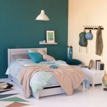small double bed with storage trundle bed rolled underneath. In emerald and cream teenager's room with gaming and skateboarding accessories