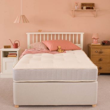 Mattress on bed with pink and brick coloured fabric and accessories. Teddy sitting on mattress