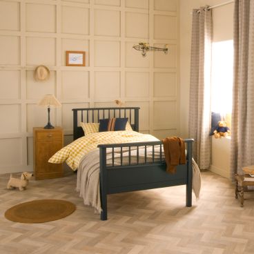 White single bed with spindles against terracotta panelled wall, next to sage green chest of drawers 