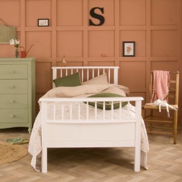 White single bed with spindles against terracotta panelled wall, next to sage green chest of drawers 