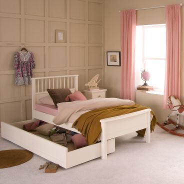 white single bed with spindles and low foot board and storage trundle underneath pulled open to show child's belongings.