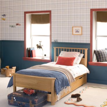 Oak single bed with trundle underneath. Bed is in a blue and red bedroom with checked wallpaper above 