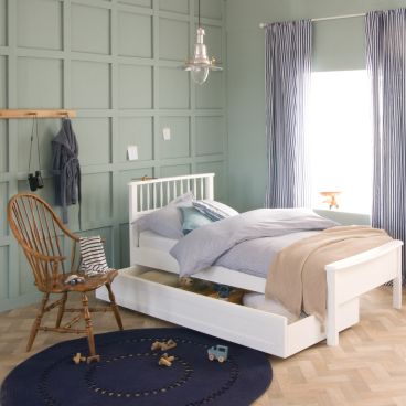 single white bed with spindles and low foot board, fishermans lamp above and wooden chair 