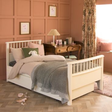 ivory white bed with spindles, with patterned curtains, terracotta panelled wall and trundle drawer and bed tucked underneath