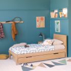 angle view of oak single linus bed with trundle pushed all the way under the bed. The bed is in a teal bedroom with orange and blue accessories
