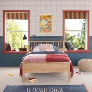 Oak small double bed with spindles, in traditional bedroom with blue panelled wall and wallpapered wall. Red architrave around windows and blue and red bedding on bed