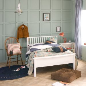 Teal blue panelled walls with white small double bed, vintage wooden chair and white bookcase.