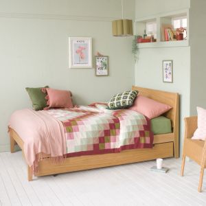 Linus oak small double bed with oak trundle underneath in a small bedroom with high windows and pink and green bedding 
