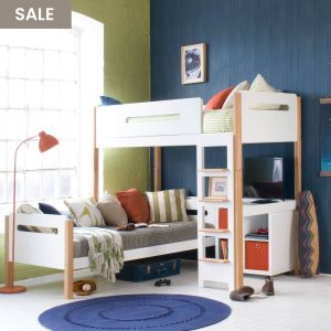 Loft bed with blue and green walls, day bed with cushions, floor standing lamp and natural bed frame. Storage unit underneath with TV screen on to the side
