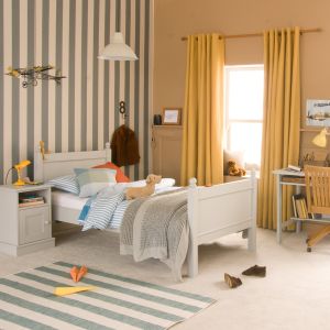 grey traditional single bed with finials with bedside cabinet and matching study desk in a caramel and green bedroom with pops of mustard and orange accessories.