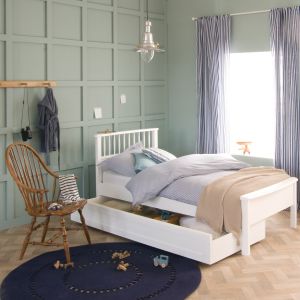 single white bed with spindles and low foot board, fishermans lamp above and wooden chair 