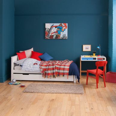 teal blue walls with comic canvas, white single bed, retro desk and red chair 